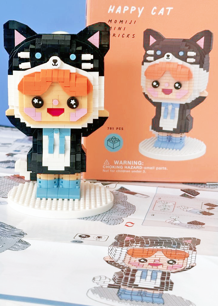 A Happy Cat Momiji doll pixel art figure stands in front of its illustrated packaging and instructions. — Momiji Doll