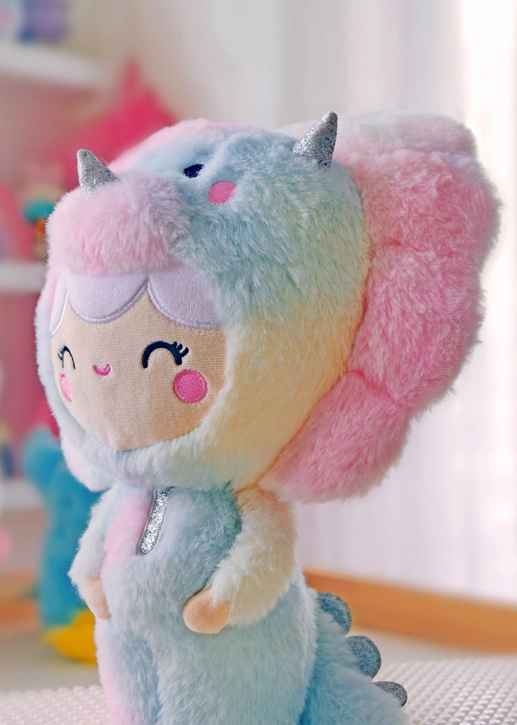 Roarsome Rainbow Plush Momiji doll with pastel blue, pink, yellow fur, dinosaur hood, silver horns, and a soft smile. — Momiji Doll