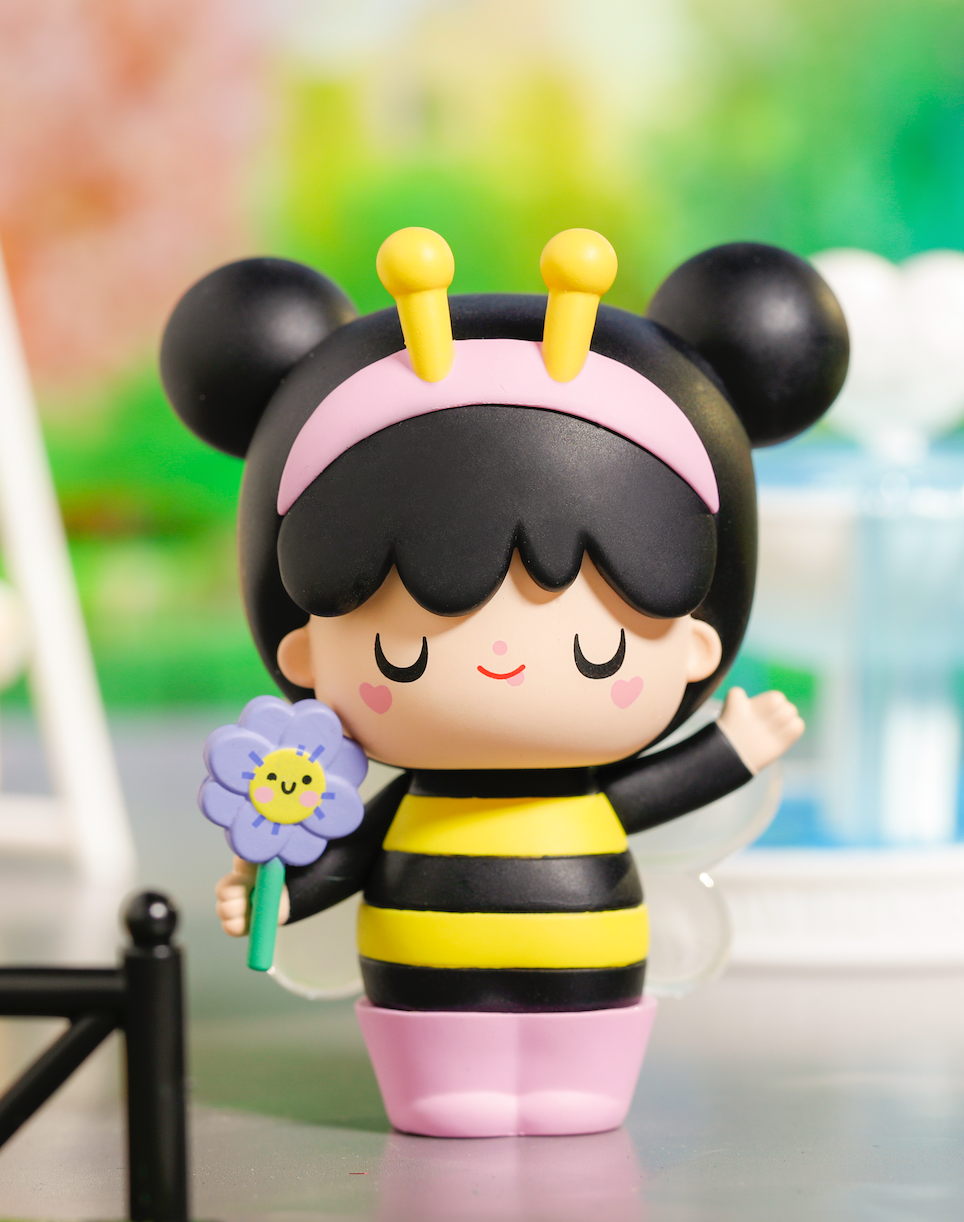 Bumble Momiji doll dressed as a bee with wings, antennae, cheerful face, and holding a smiling flower. — Momiji Doll