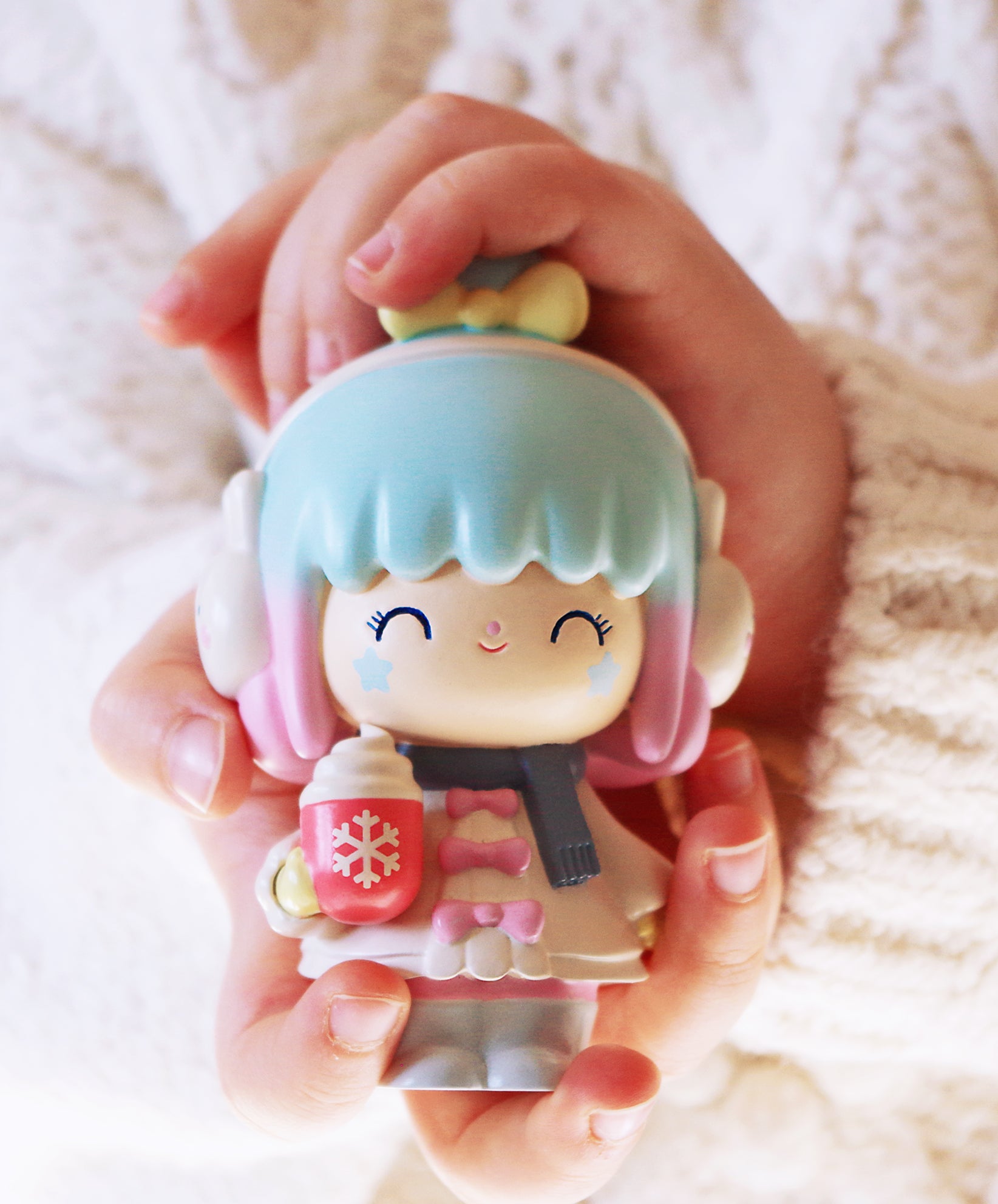 A person holds the Winter Wonderland 2020 Momiji doll with blue hair, earmuffs, and a pastel mug; vinyl collectible with secret message. — Momiji Doll
