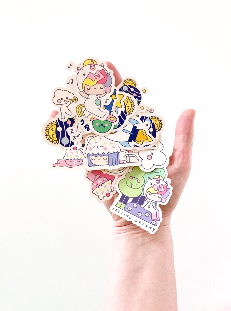 A hand holds Happy Days Momiji doll stickers featuring unicorns, clouds, and other adorable kawaii cartoon characters. — Momiji Doll