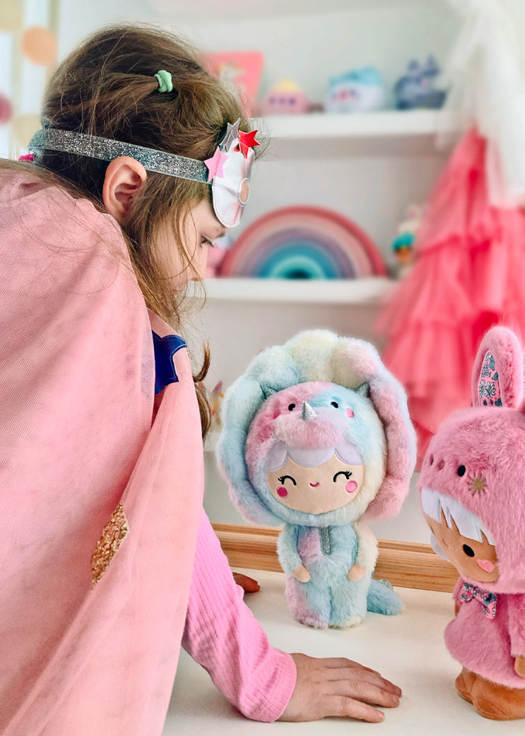 A Momiji doll with a pink cape and mask plays with the Roarsome Rainbow plush in a bright, whimsical room. — Momiji Doll