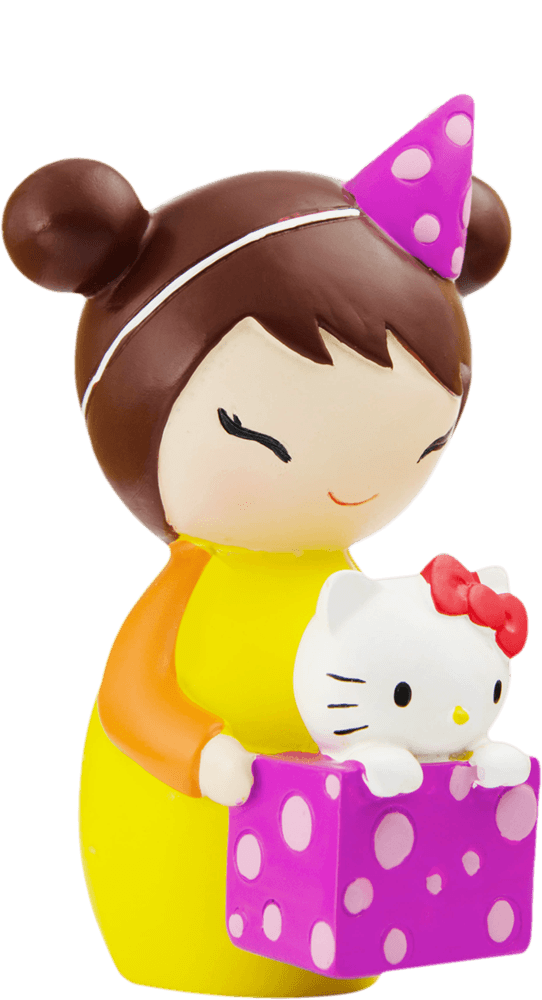 A smiling girl in a party hat holds a pink polka-dot box with a kawaii Kipi Momiji doll inside. — Momiji Doll