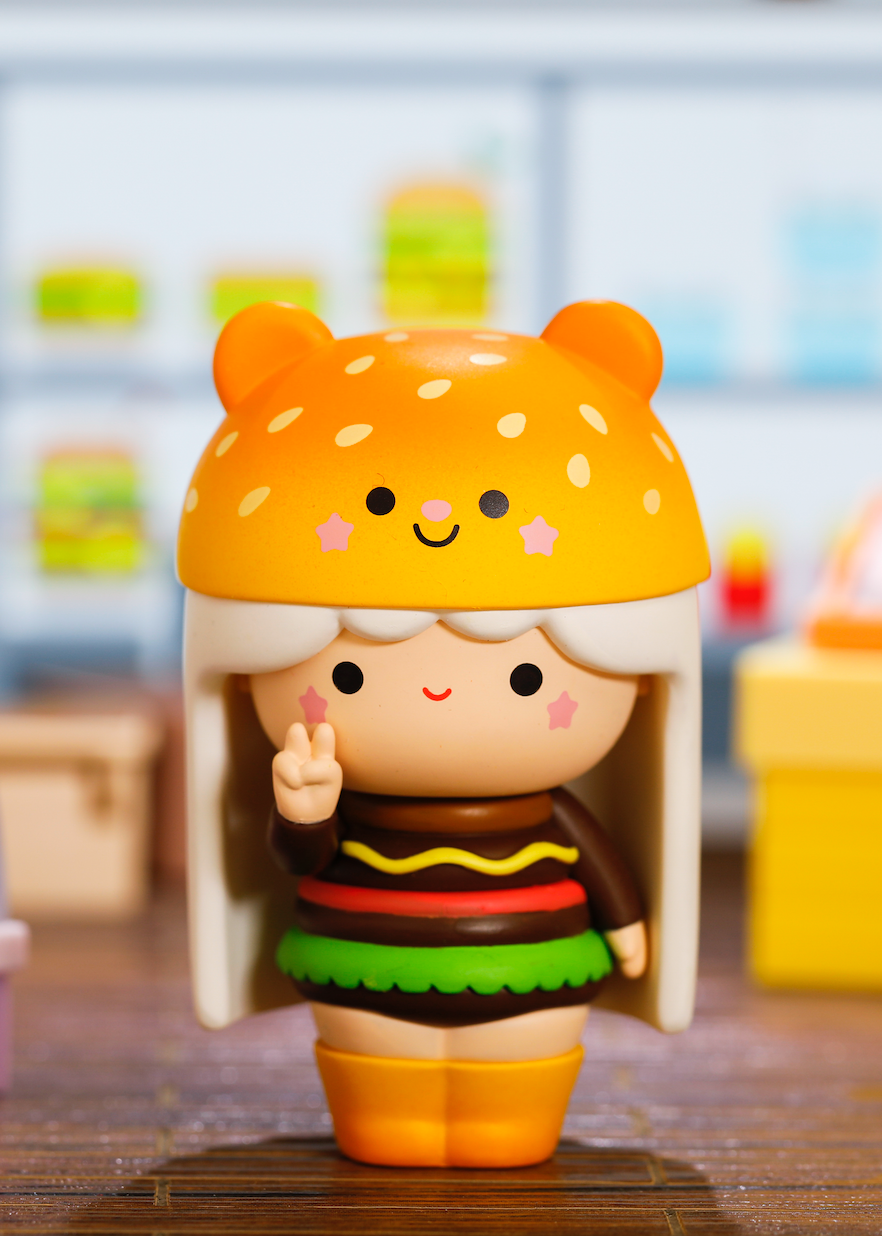 The Perfect Partners Momiji doll wears a burger suit with bear bun hat, making a peace sign. Kawaii vinyl collectible indoors. — Momiji Doll